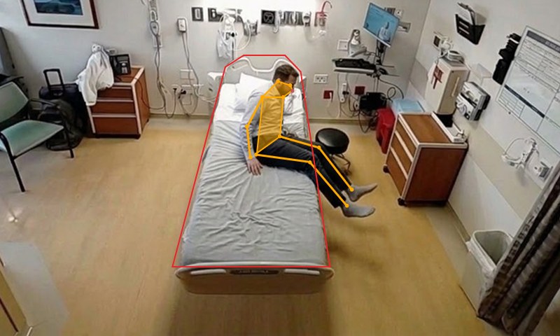 Patient sitting on the edge of the bed, past the boundary drawn in red, with pose tracking overlaid